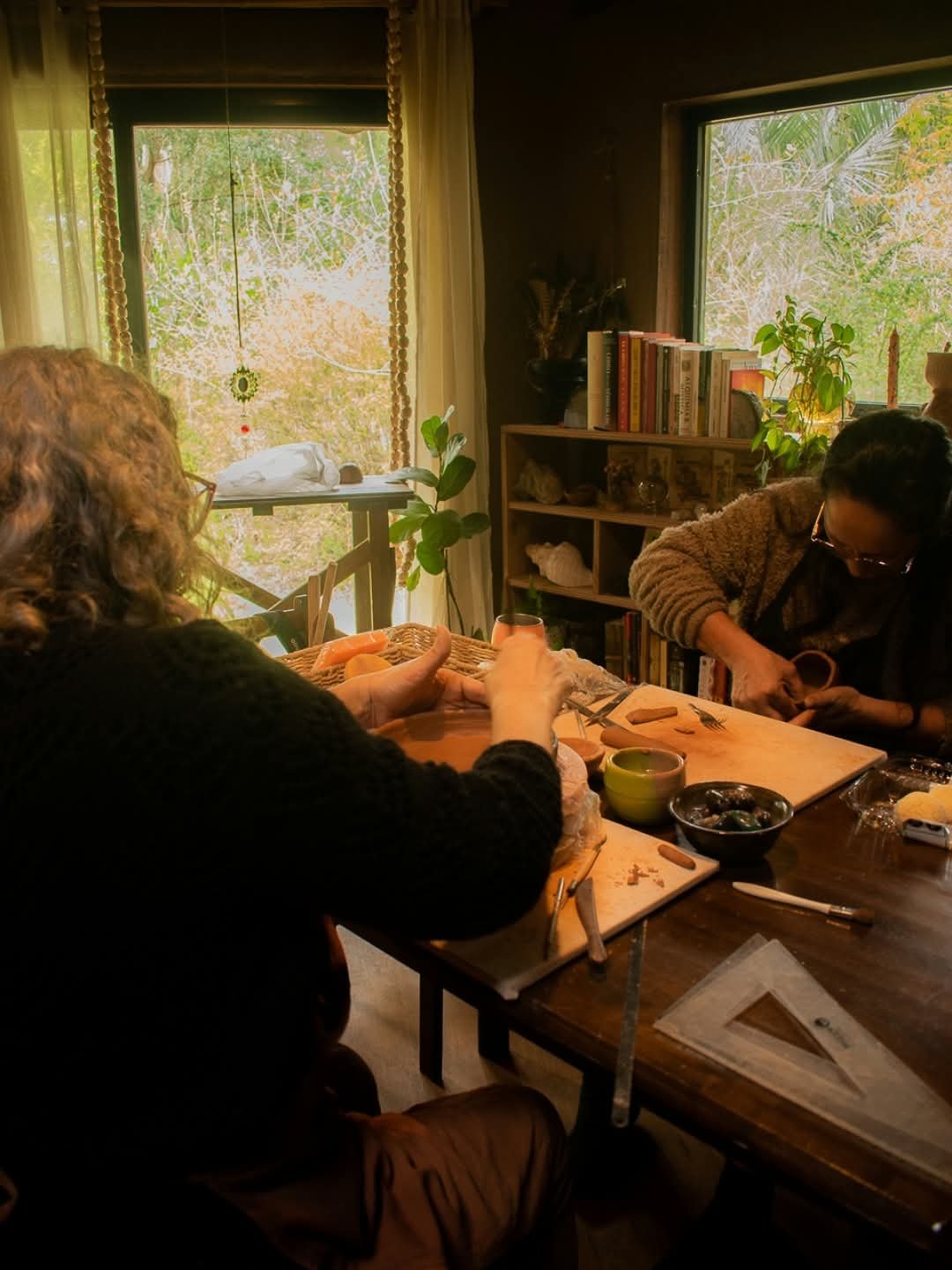 Dos personas modelando arcilla en una mesa de trabajo junto a la ventana